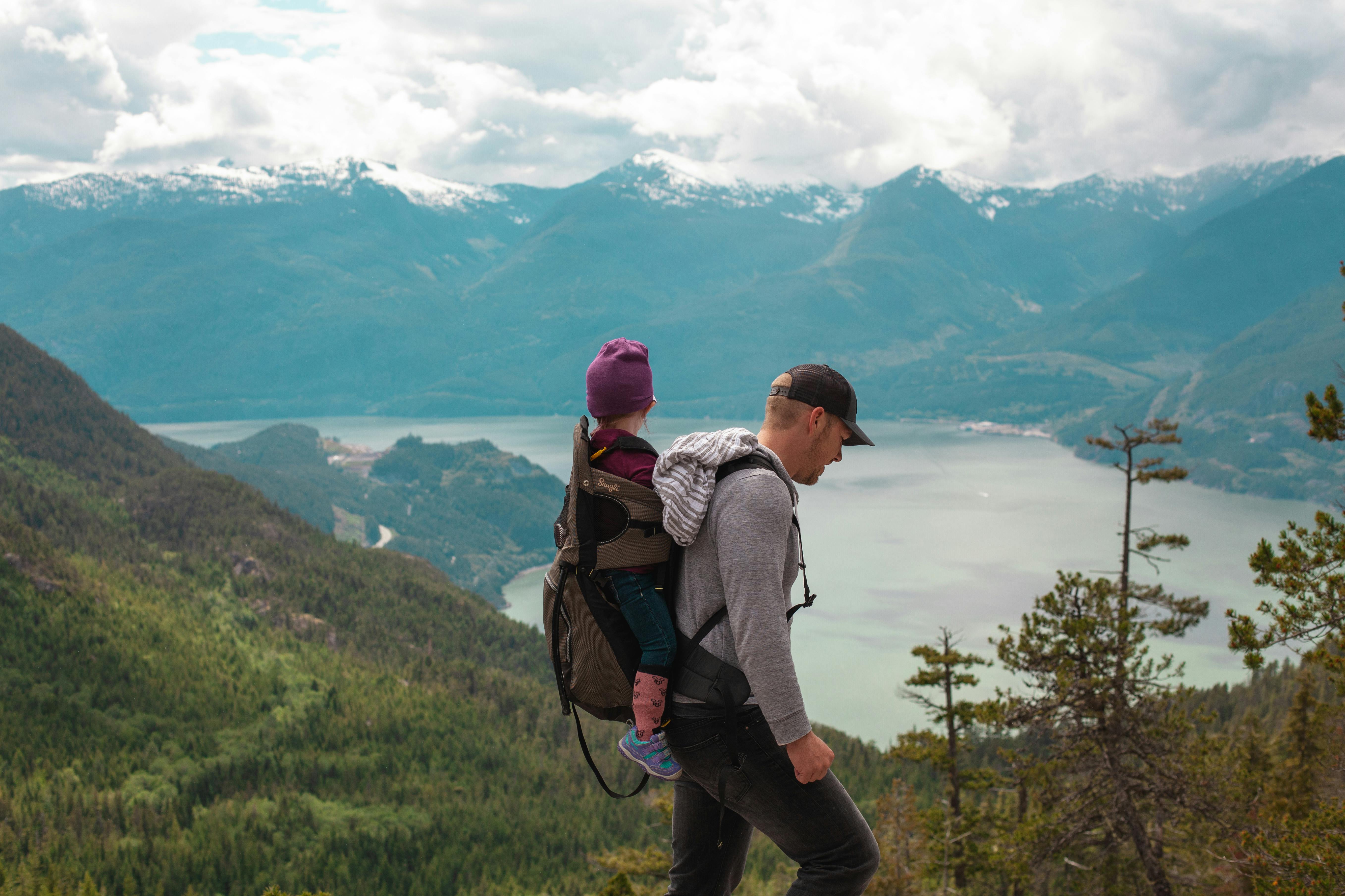 A dad with baby toddler rear carrier hiking with natural landscape in the background