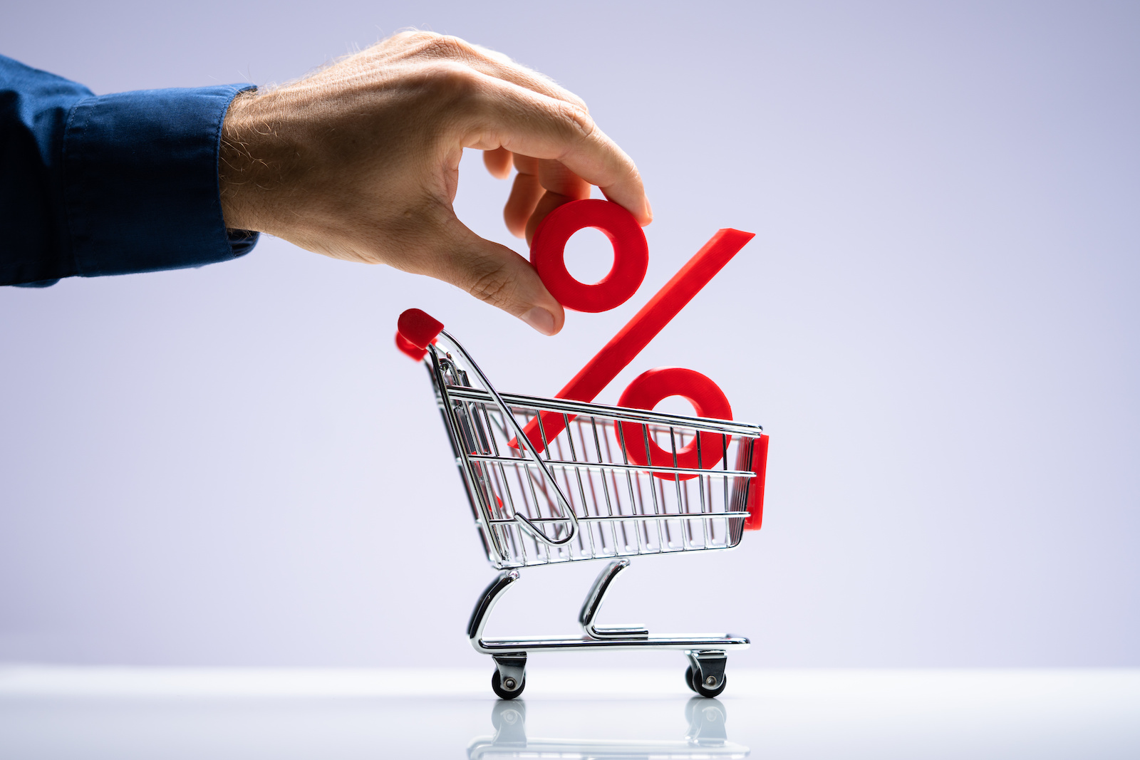 Hand placing a red percent sign into a mini shopping cart