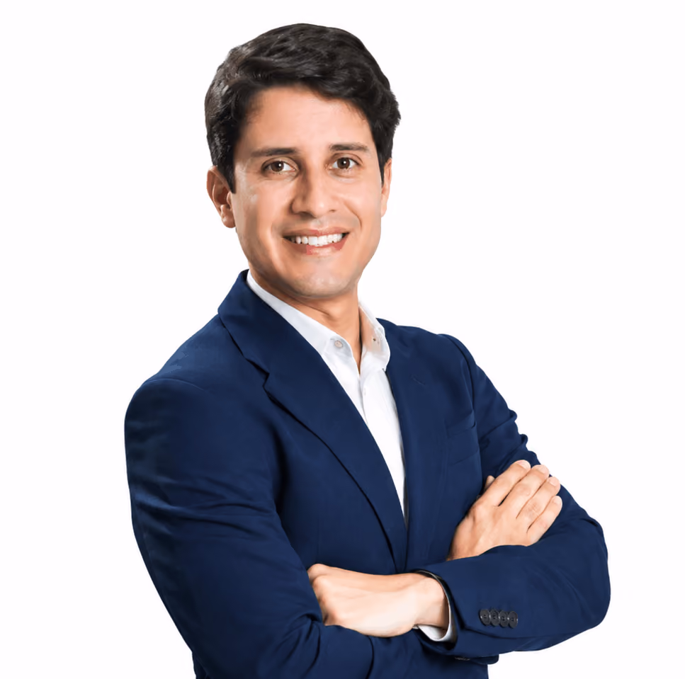Smiling man with dark hair in a blue suit jacket and white shirt, arms crossed, on white background.
