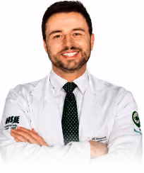 Smiling man with short hair wearing a white lab coat and black tie, arms crossed.
