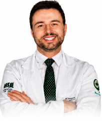 Smiling man with short hair wearing a white lab coat and black tie, arms crossed.