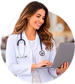 Smiling female doctor in white coat using a laptop with stethoscope around her neck.