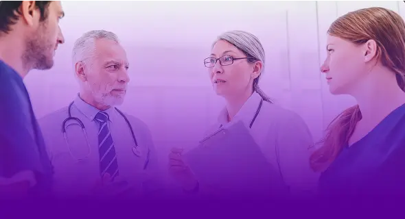Grupo de quatro médicos de jaleco e uniforme conversando em pé