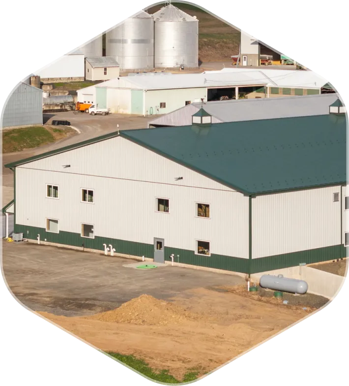 Large agricultural building with green roof and silos in the background on a farm.