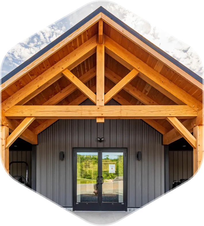 Entrance with double glass doors under a wooden timber frame roof and gray metal siding walls.