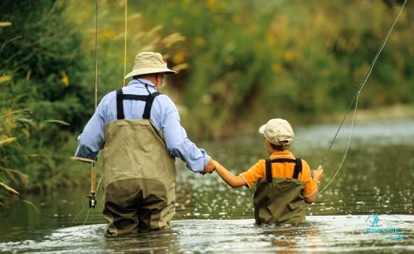 Een man (waarschijnlijk grootvader) die met een kind doorheen het wateren aan het lopen is om te kunnen vliegvissen