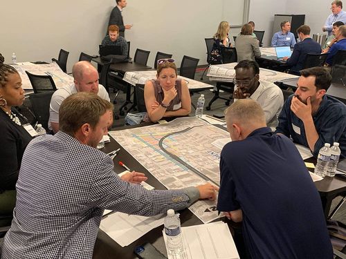 A group of stakeholders sitting at a table discussing a design concept shown on a roll plot during a stakeholder advisory committee meeting.
