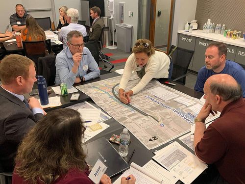 A group of stakeholders sitting at a table discussing a design concept shown on a roll plot during a business advisory committee meeting.
