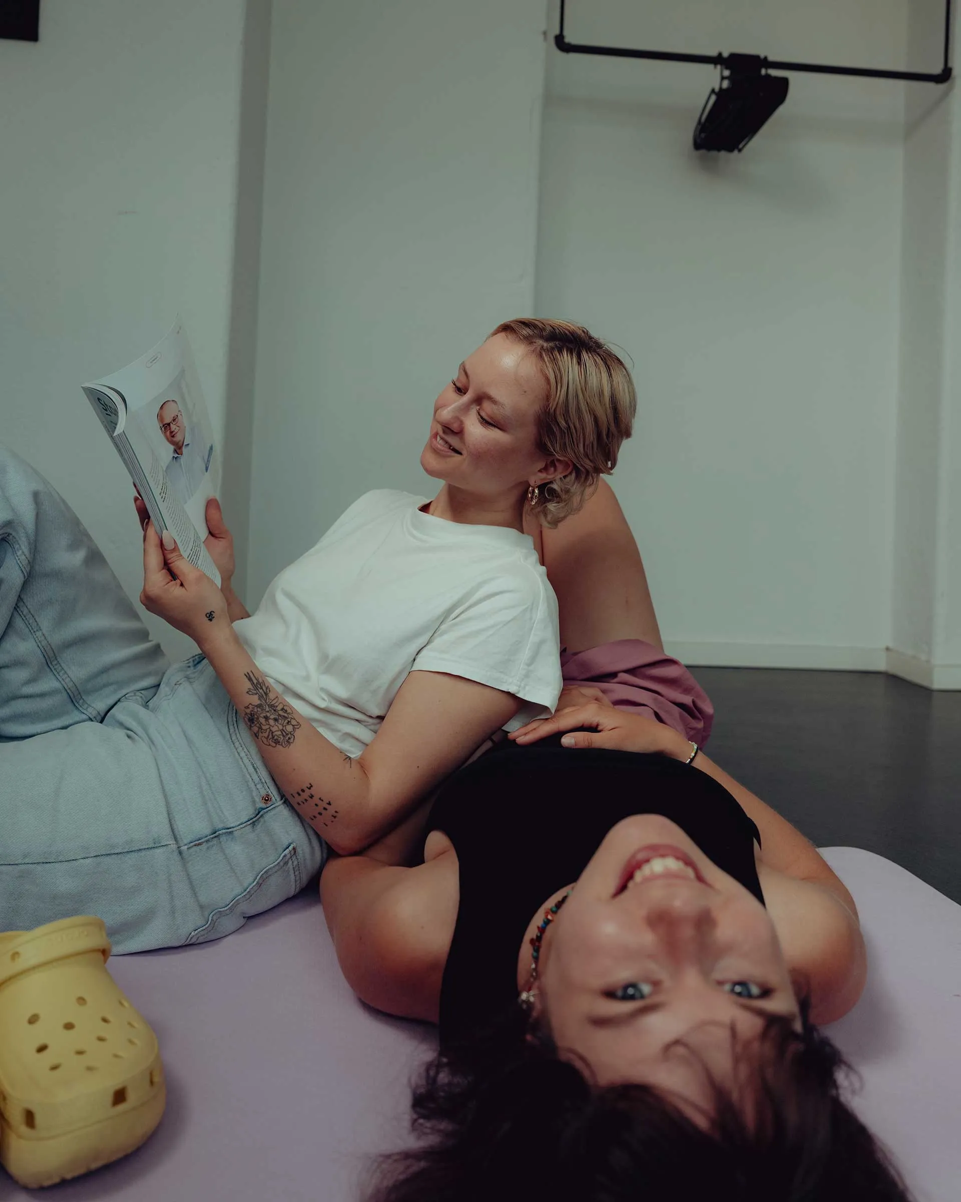 Two young women lounging on the floor, one reading a magazine and the other smiling at the camera.