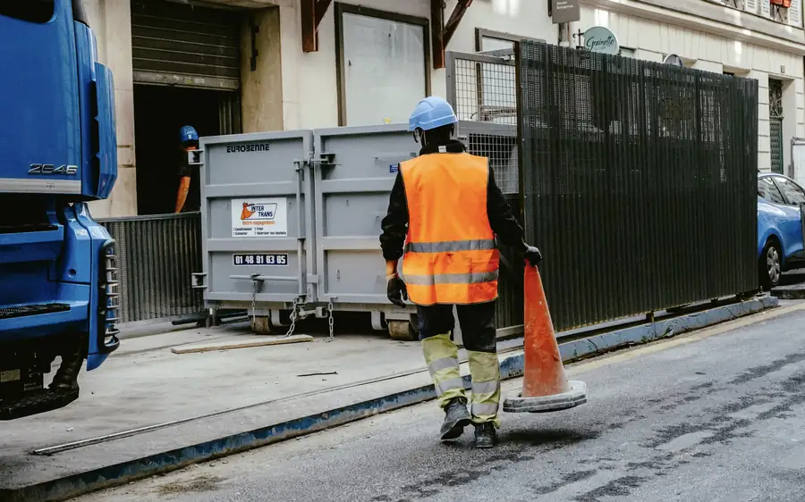 Contractor in hi-vis vest carrying a traffic cone at street works