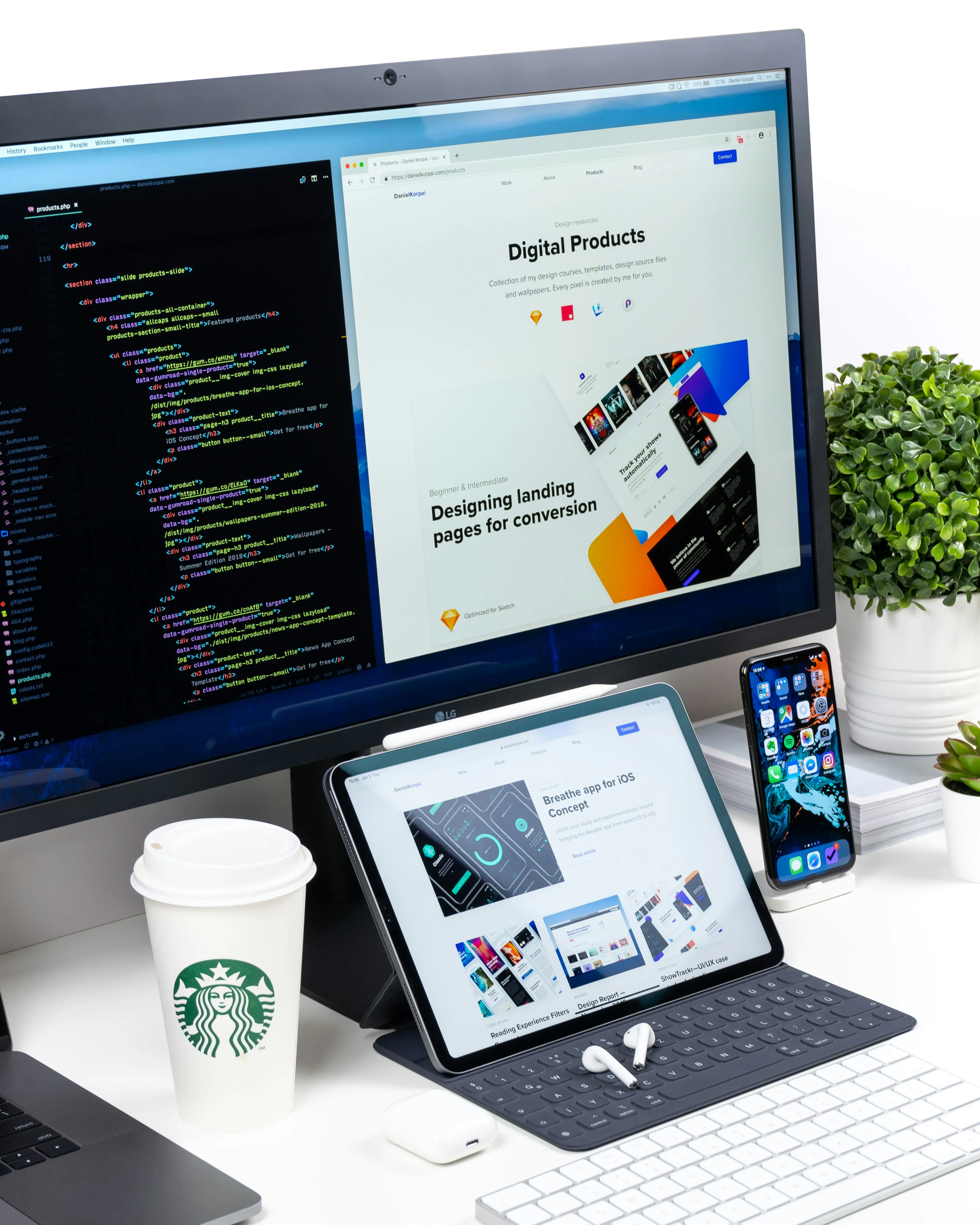Nowoczesne stanowisko pracy projektanta z monitorem wyświetlającym kod HTML i stronę produktową, tabletem z aplikacjami do projektowania, smartfonem, klawiaturą, AirPods, filiżanką kawy Starbucks i zieloną rośliną na biurku.