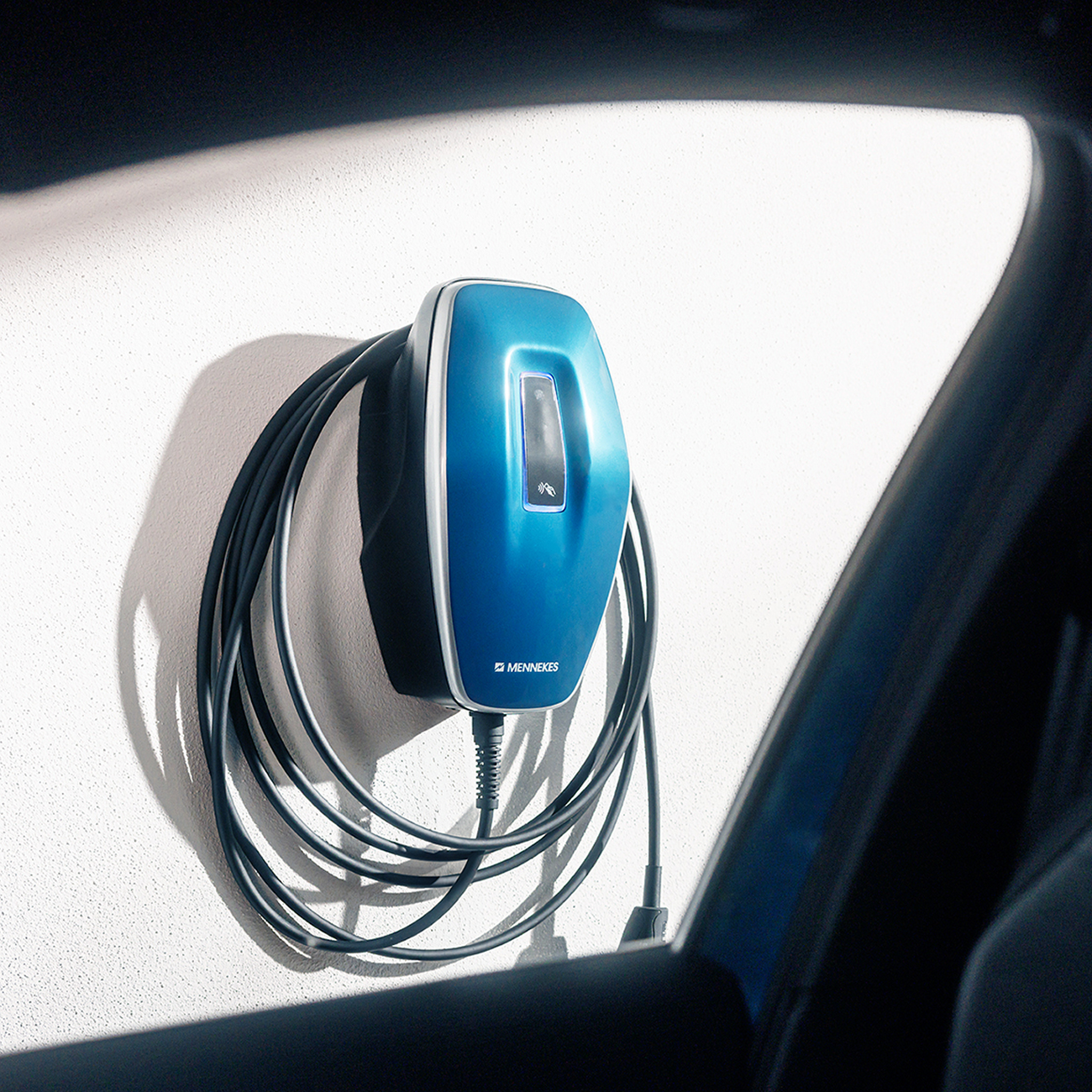 Blaue Wallbox mit Ladekabel an weißer Garagenwand – intelligente Ladelösung für Elektrofahrzeuge im Eigenheim.