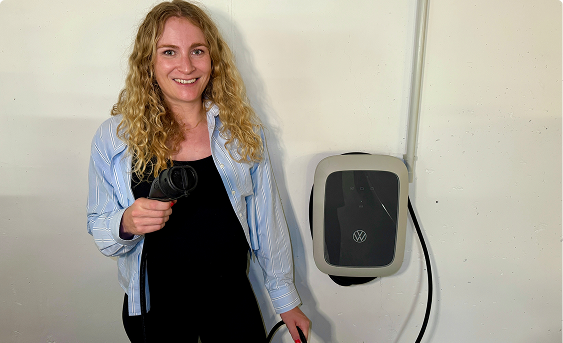 Zufriedene Frau mit Ladekabel vor VW-Wallbox in der Garage – moderne Ladelösung für Elektroautos im Eigenheim.
