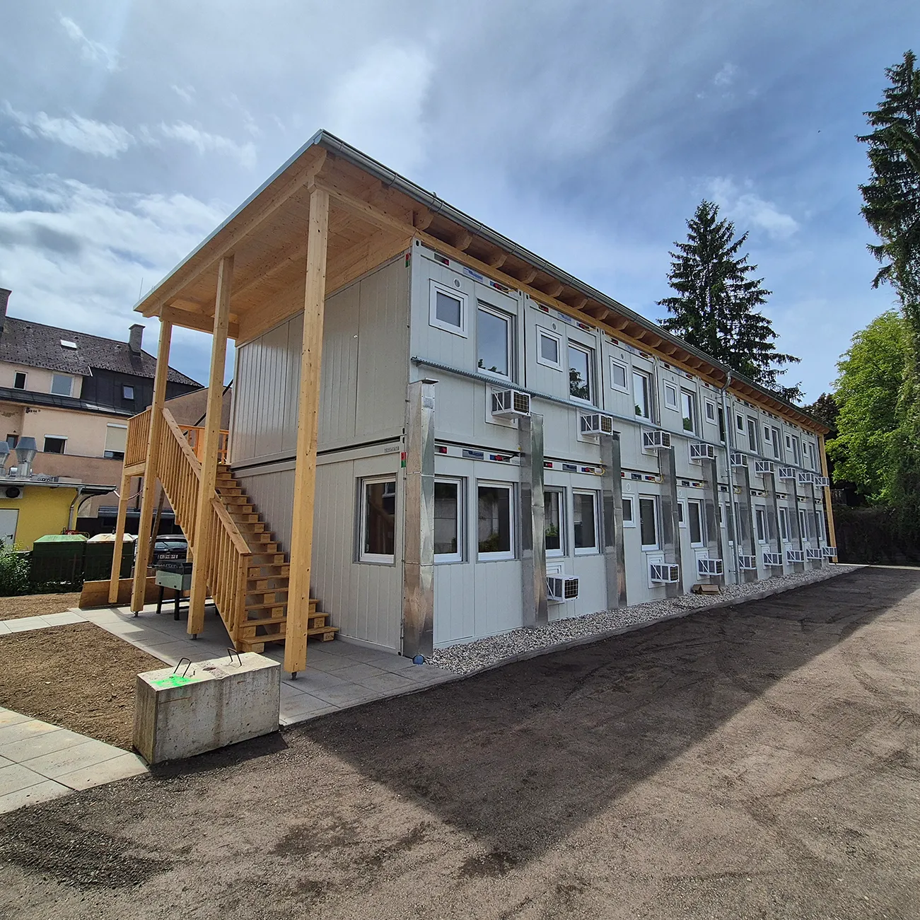 Zweistöckiges Wohncontainergebäude mit Außentreppe aus Holz und mehreren Klimageräten an den Fenstern.
