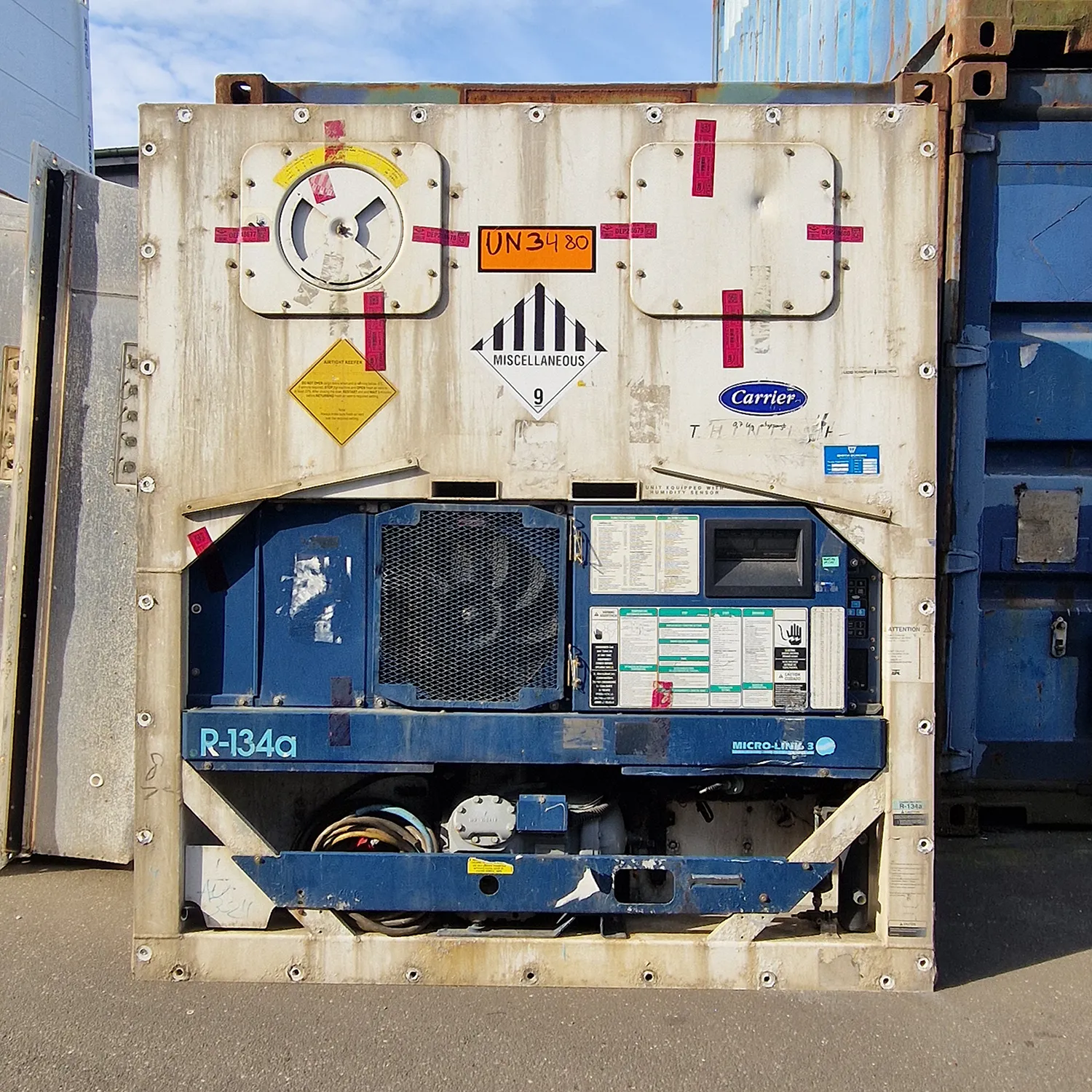Frontansicht eines weißen Kühlaggregats an einem Container mit blauen technischen Komponenten und Warnaufklebern.