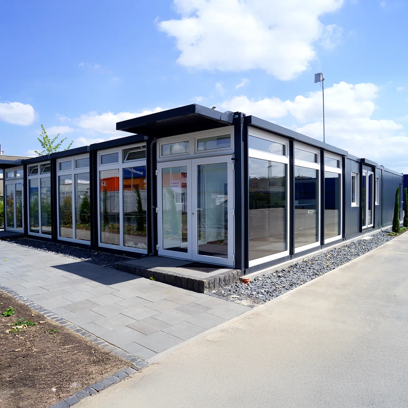 Modulare Containeranlage mit großen Fensterflächen und Flachdach unter blauem Himmel.
