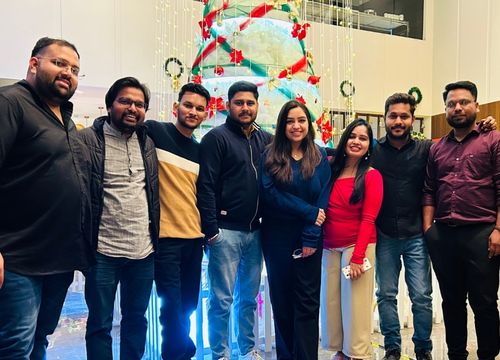 Group of seven people smiling and posing for a photo indoors with warm lighting.