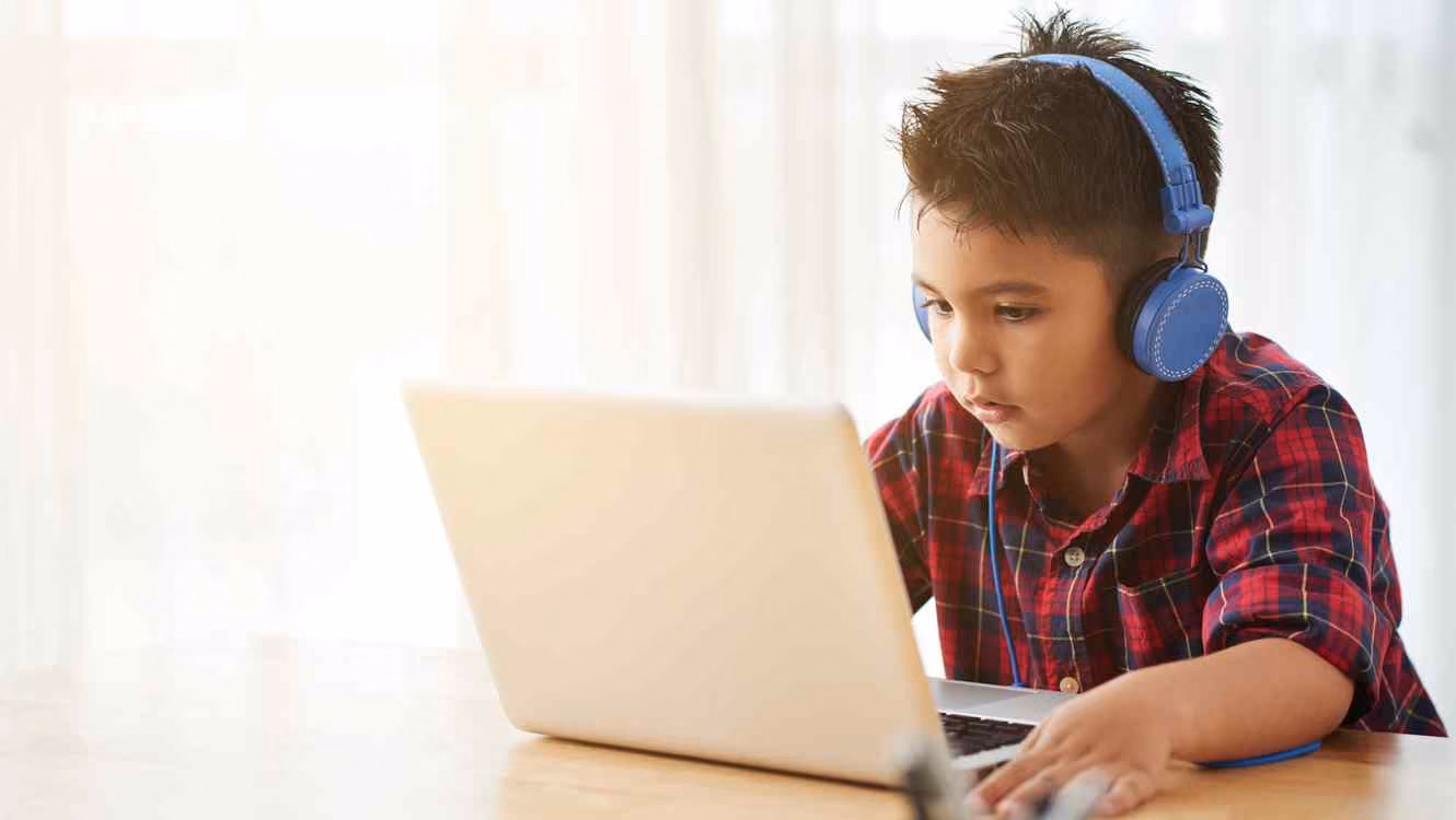 Un niño usando audífonos mientras usa una computadora