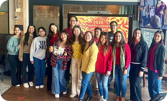 A group of people smiling for a photo in front of a 2026 Lunar New Year poster.