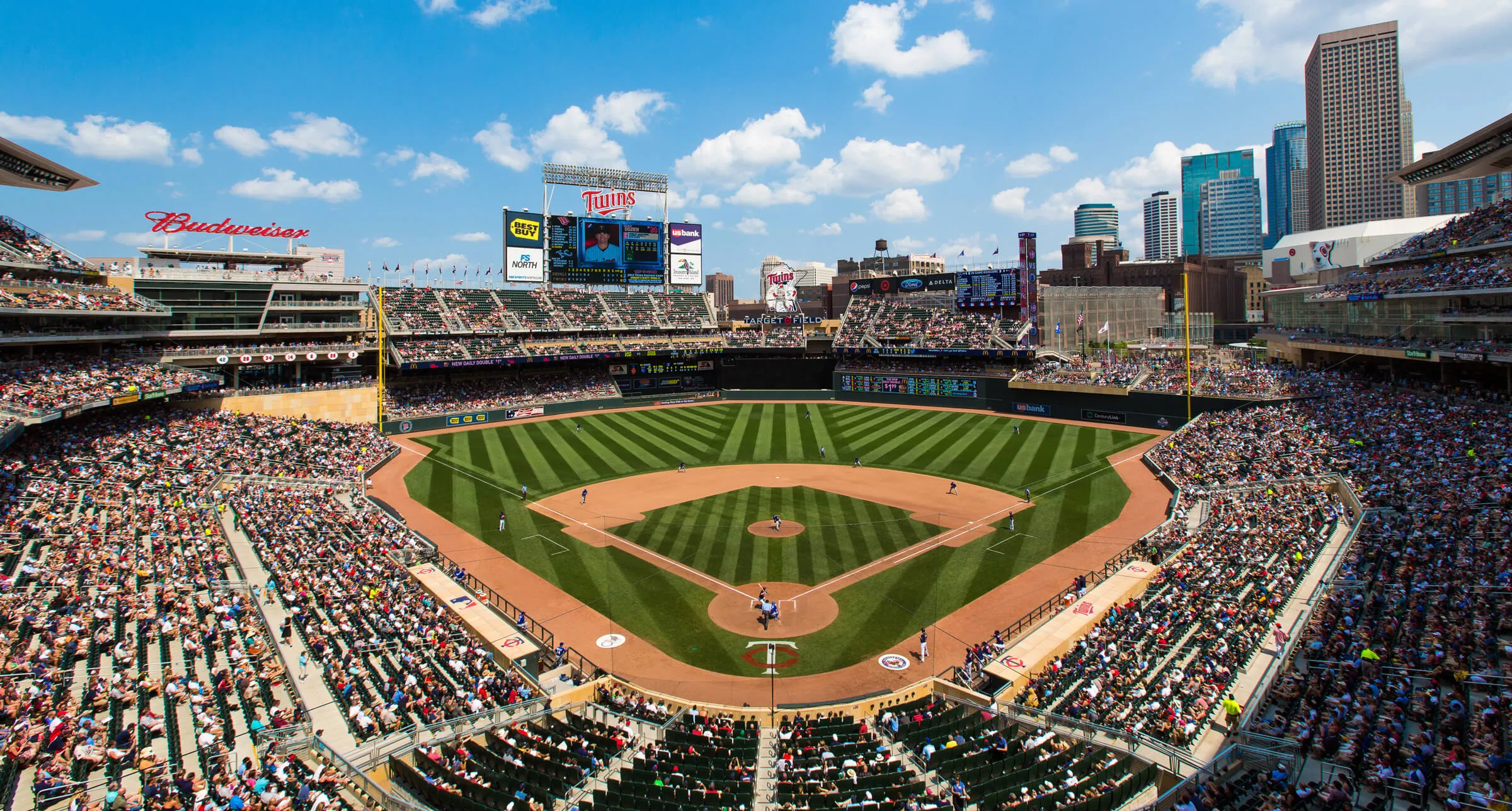 Wide view of a baseball game at Target Field with spectators and city skyline under blue sky.