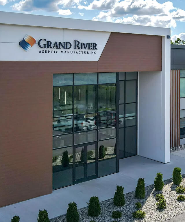 Modern building entrance with glass doors and sign reading Grand River Aseptic Manufacturing.