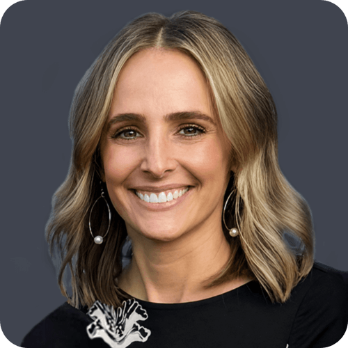 Smiling woman with shoulder-length blonde hair wearing pearl earrings and a black top with floral detail.