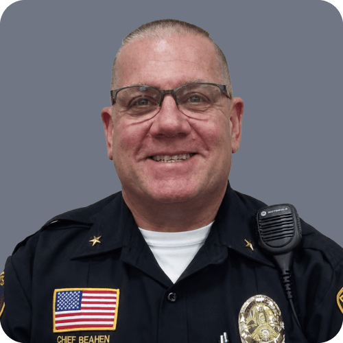 Jeff Beahen. A smiling police officer with glasses in uniform, American flag patch, badge, and radio microphone.