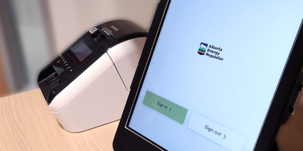 Tablet screen displaying the Alberta Energy Regulator logo with two buttons labeled 'Sign in' and 'Sign out,' beside a label printer on a wooden surface.