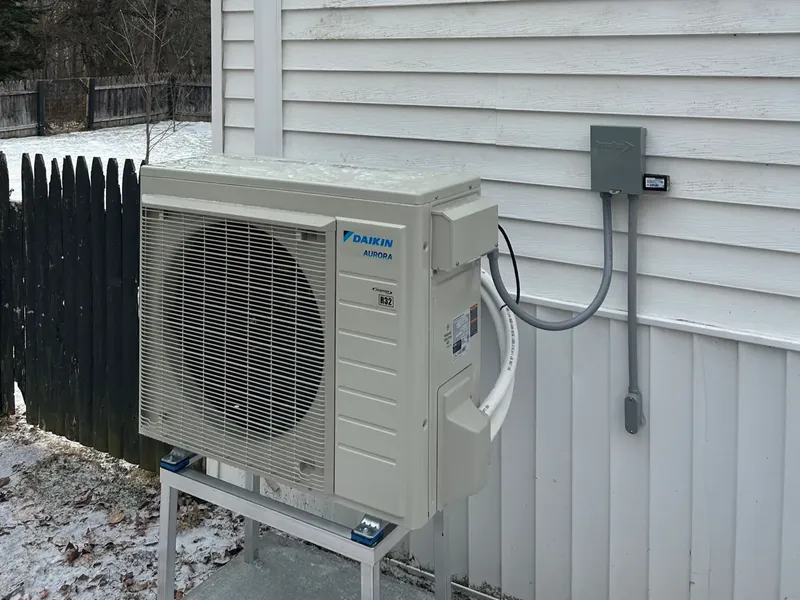 Daikin outdoor unit with disconnect, protected lineset and raised stand.