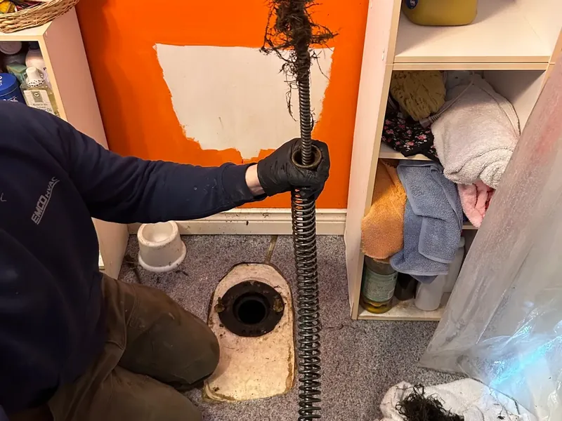 Roots on a drain auger beside an opened sewer drain.