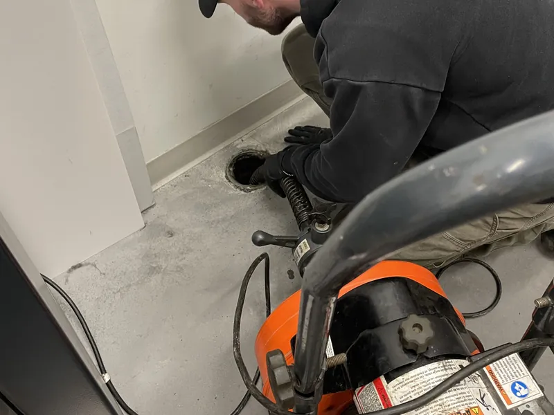 Plumbing technician feeding a drain-cleaning cable into a floor drain.