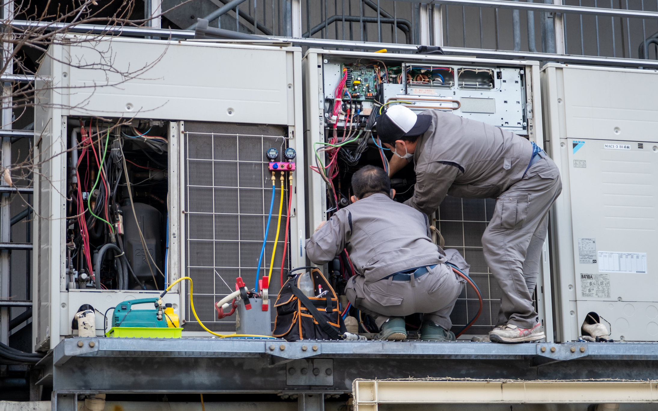HVAC technicians carefully reconnects wires in AC unit.