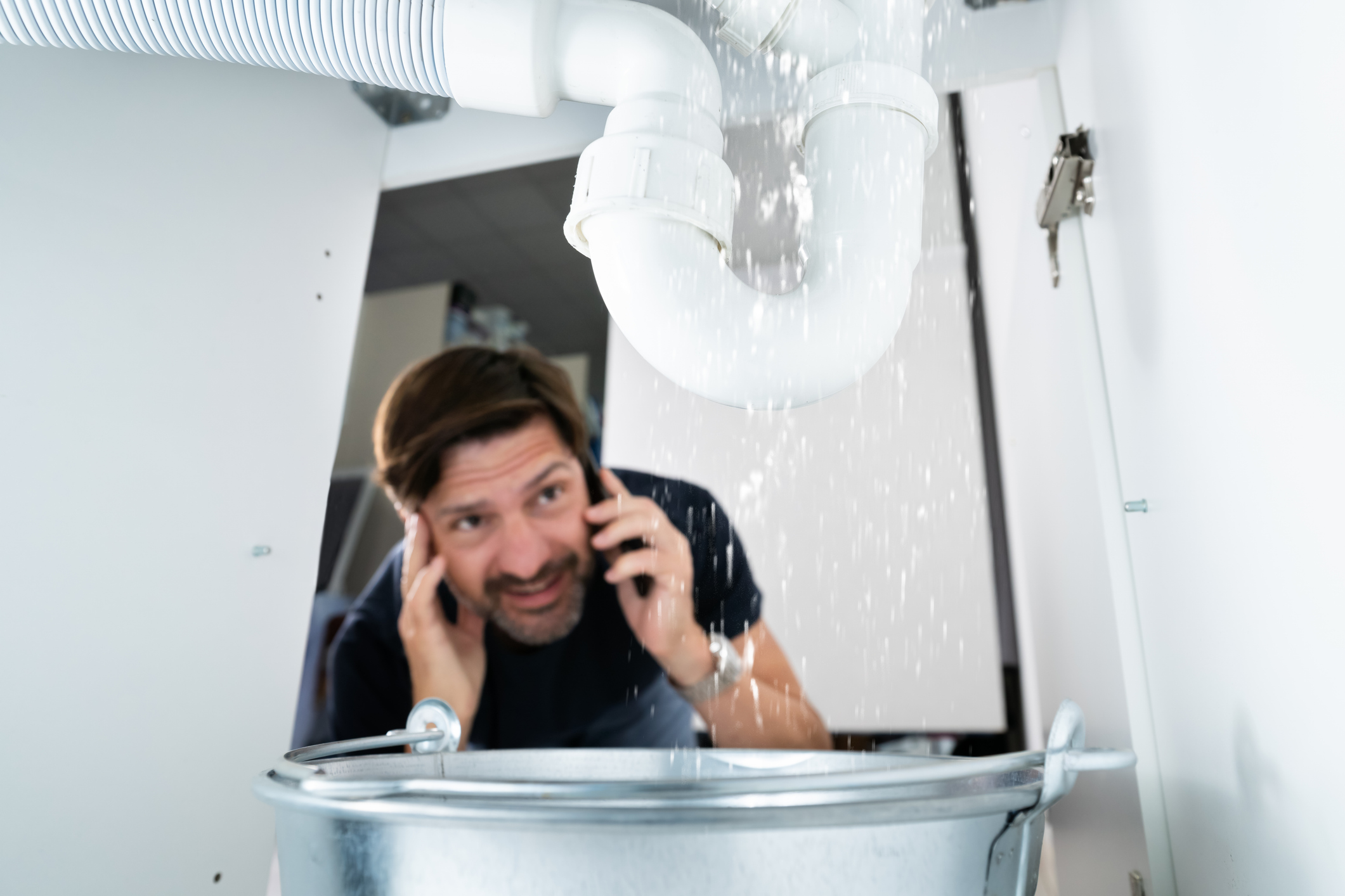 A homeowner calling a plumbing company to fix leaks in his kitchen.