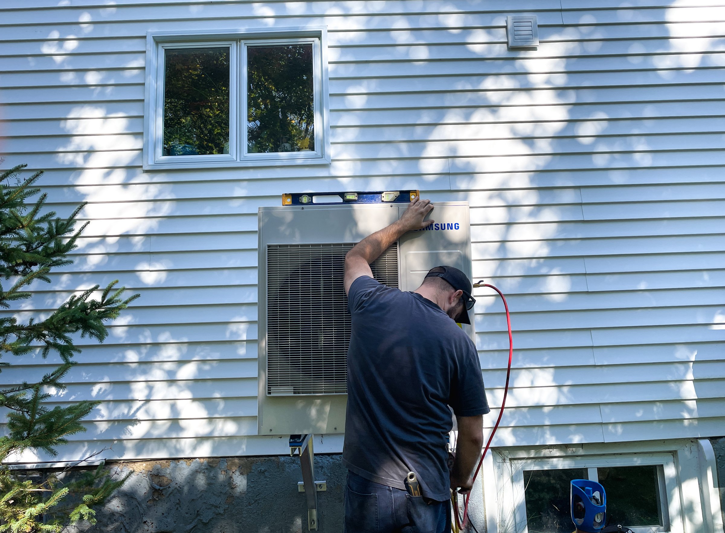 Matrix Mechanical technician levelling a wall-mounted heat pump outdoor unit during installation