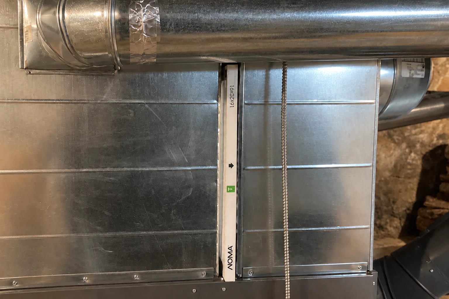 Air filter in a rack between sheet-metal duct sections above an air handler.
