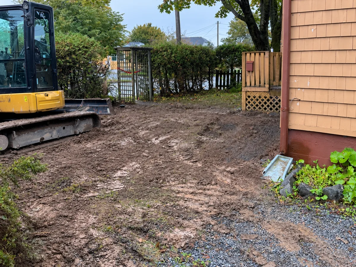 Backfilled soil beside the house and excavator after the sewer and water-service work.