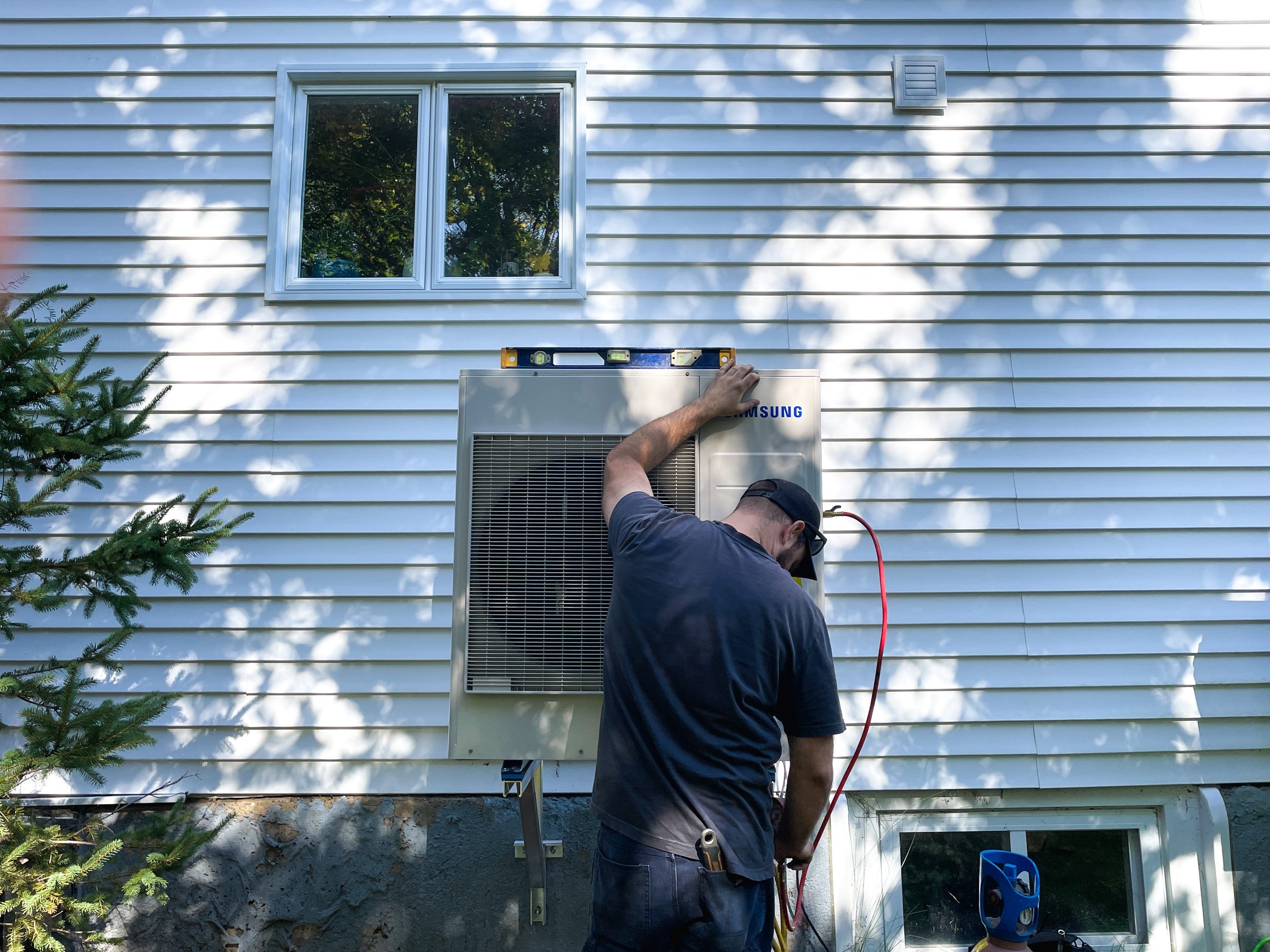Matrix technician working beside outdoor heat-pump equipment at a home.