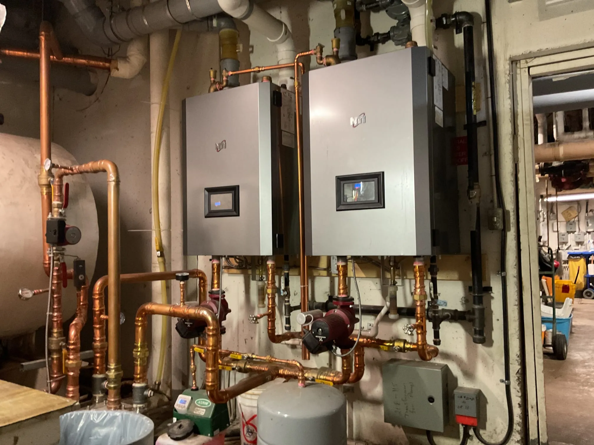 Two wall-mounted boilers and the distribution piping a heating contractor assesses.