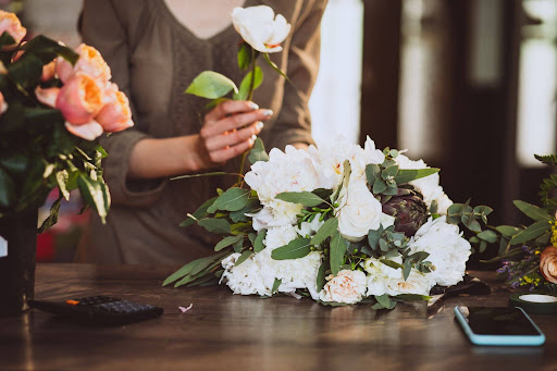 Florist arranging fresh flower bouquet on worktable, selecting stems and greenery while creating a decorative floral arrangement in a shop