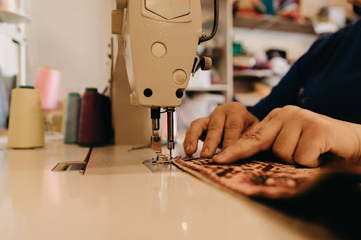 Hands operating sewing machine stitching fabric, close-up of tailoring work with thread spools in workshop setting