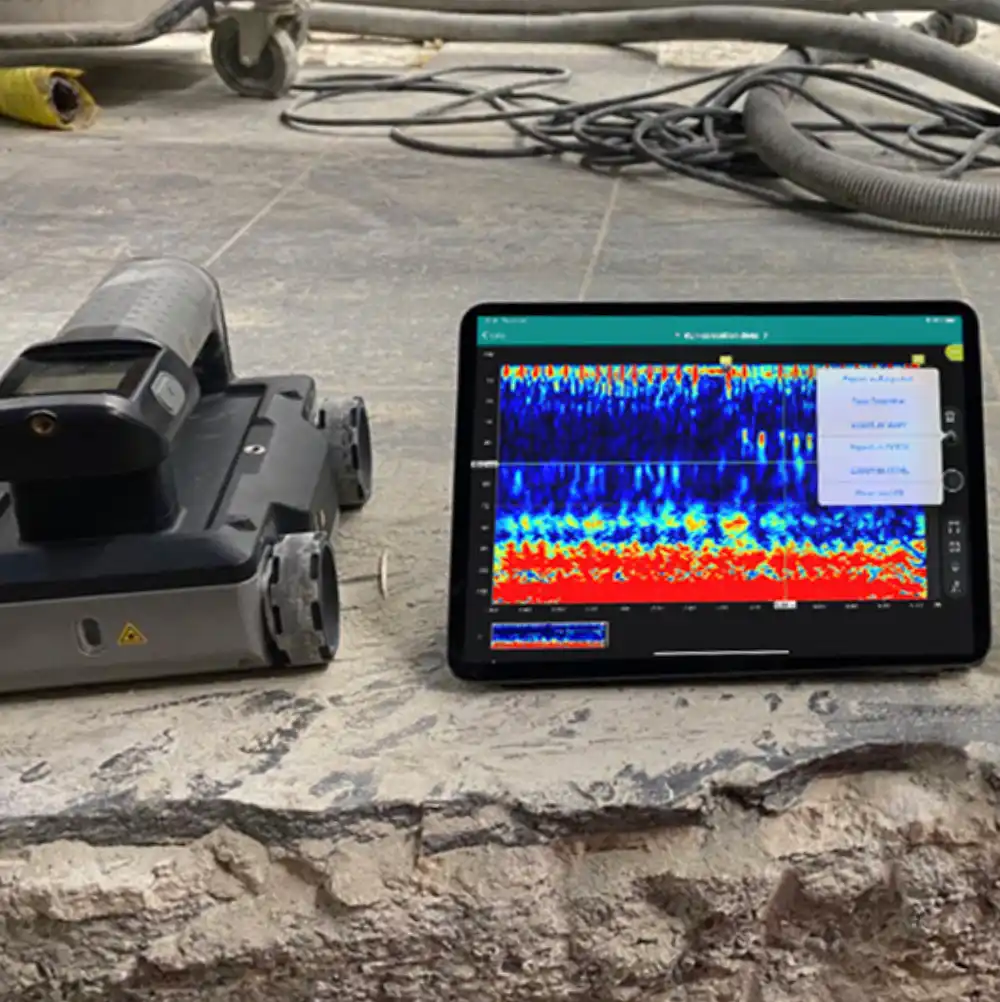 A GP8000 scanner sits next to an application showing migrated GPR data on the edge of a broken, tiled concrete slab.