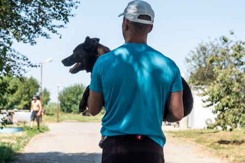 Доброволец, заснет в гръб, носи средно по размер тъмно кафяво куче на ръце.