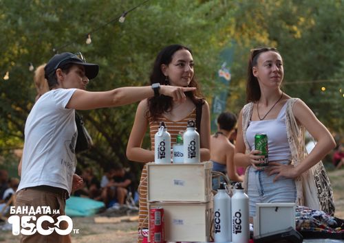 Трима души стоят покрай маса с нареден мърч на нея.