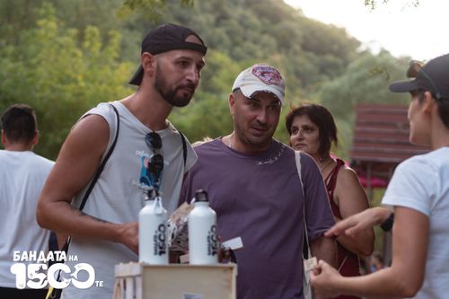 Двама младежи облечени в бял потник и лилава тениска говорят с доброволец на щанда на Бандата на 1500-те.