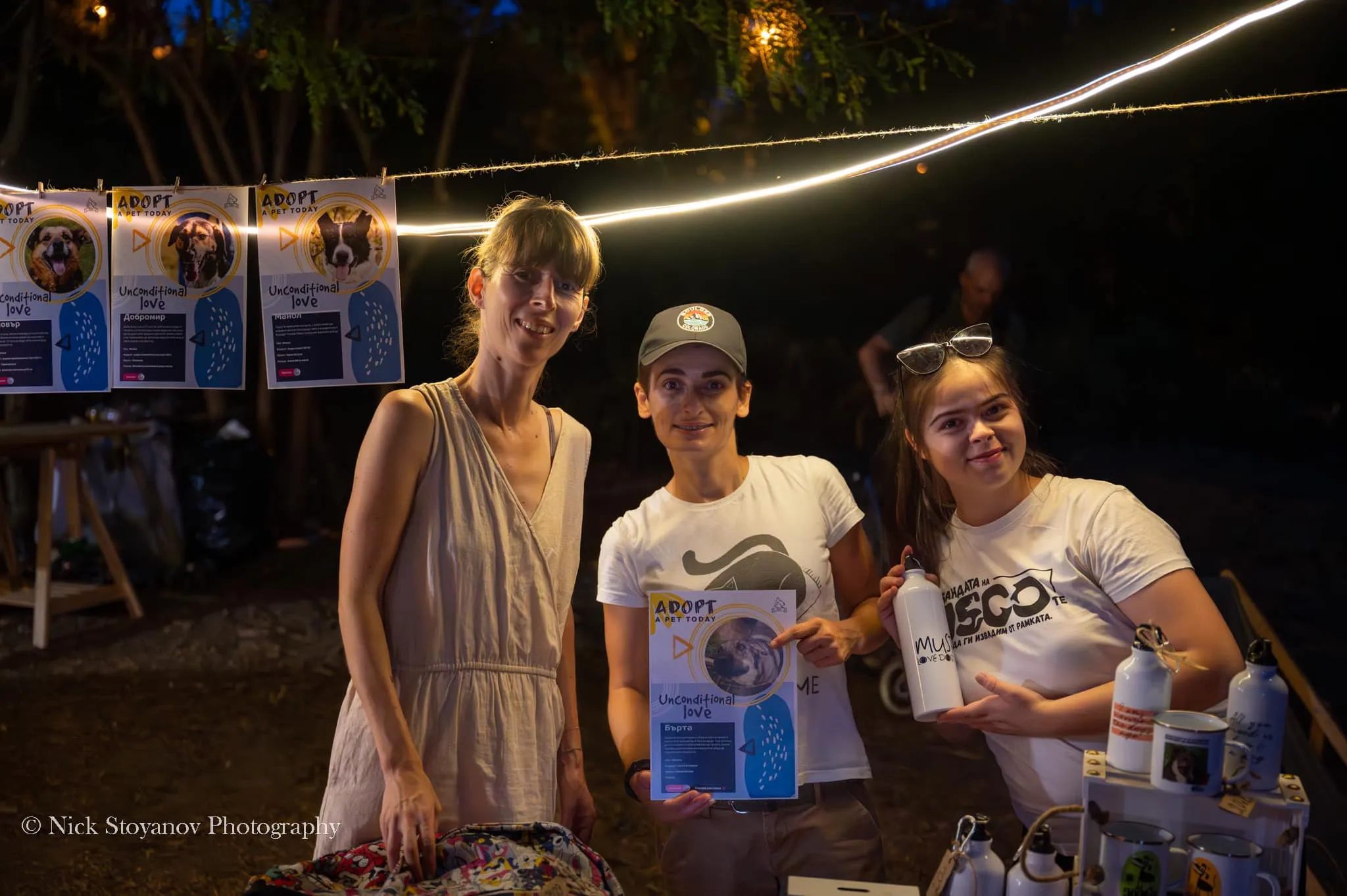 A group of female volunteers pose for a photo at their boot, holding items promoting adoption and pet care.