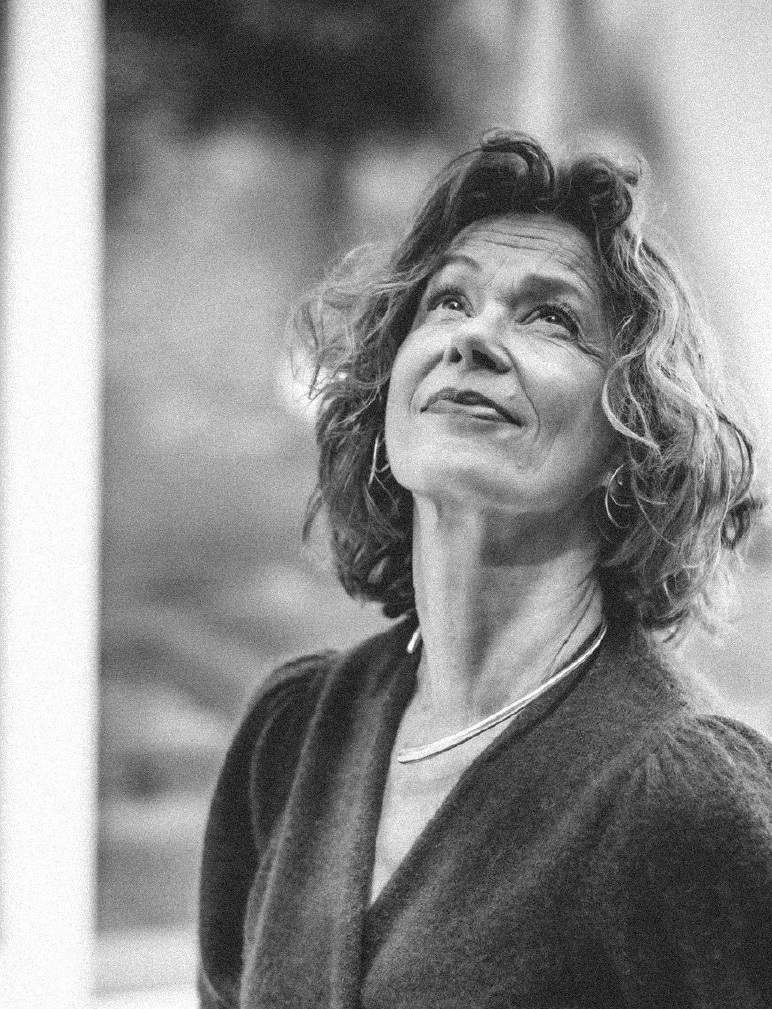 Black and white close-up of Liesbeth Dillen in nature, looking up at the sky with a gentle smile