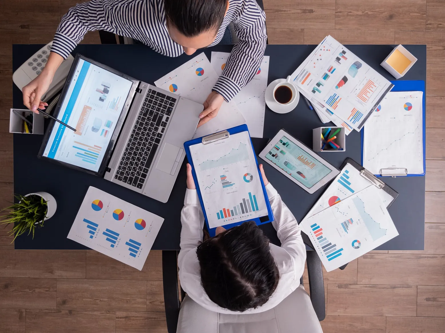 Vista de cima de duas pessoas analisando relatórios e gráficos na mesa