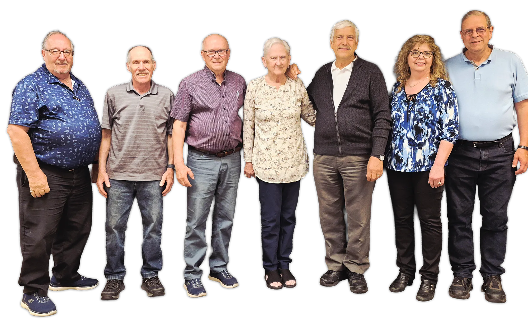 Group of seven older adults standing in a row, casually dressed, smiling at the camera.
