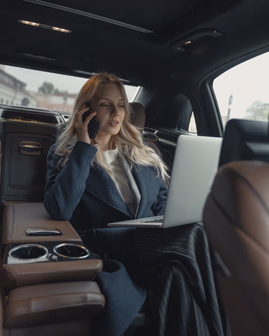 Woman being driven in luxury car while using computer and speaking on a cell phone