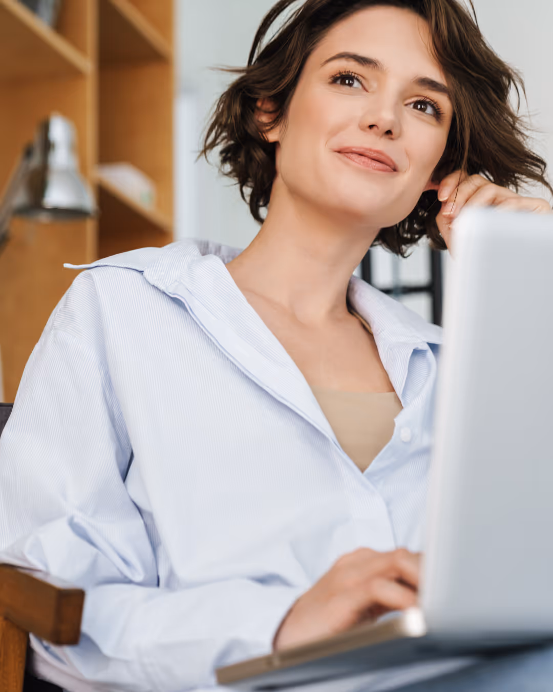 woman in a button down working on laptop in her lap